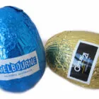 Two foil-wrapped chocolate eggs, one blue and one gold, with logo labels on each.