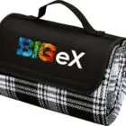 A folded picnic blanket with a plaid pattern featuring black, white, and grey colors. It has a black flap with a handle and the word BigEx in colorful letters printed on it.
