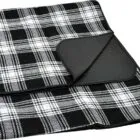 A folded black and white plaid picnic blanket with a black backing. The blanket features a classic checkered design and is neatly arranged to show both the patterned and solid sides.