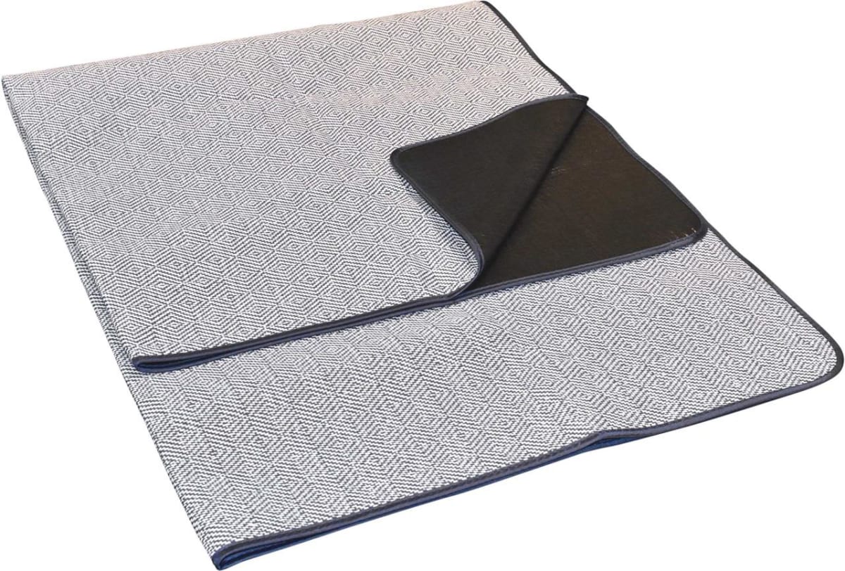 A folded picnic blanket with a geometric pattern in white and gray on one side and solid black on the other. It has a blue trim around the edges. The blanket is spread out on a white background.