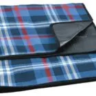 A folded picnic blanket with a blue, red, and white plaid pattern. The underside is black and appears waterproof.