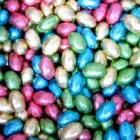 Colorful, foil-wrapped chocolate eggs in pink, blue, green, and silver, scattered close together.