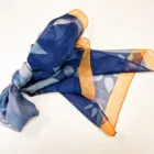 Blue patterned scarf with orange edges, loosely tied, on a white background.