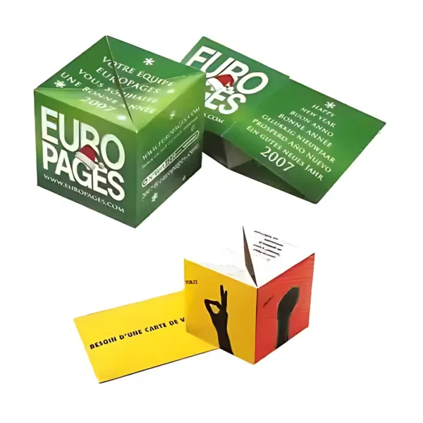 Two promotional Fold Out Paper Cubes 8cm Big from EUROPAGES feature vibrant designs in French. The top cube is green with bold white EUROPAGES text, while the bottom cube combines yellow and red, displaying a hand gesture graphic and additional details.