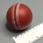 A Promotional Stress Ball Cricket Red is placed on a flat surface next to a white ruler with centimeter and millimeter markings. Its prominent stitching adds an elegant touch, making it ideal for promotional displays.