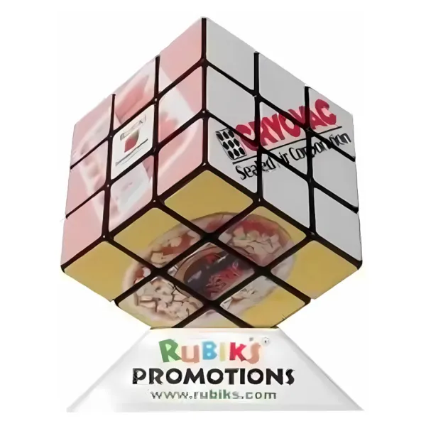 A Rubiks 3x3 Cube features promotional images on each face, mounted on a Rubiks Promotions stand with different product showcases and a website URL below.