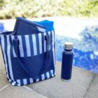 Blue-striped tote and blue water bottle beside a pool on a sunny day.