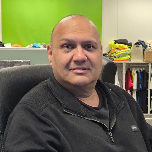 A man in a black sweater sits at the Sydney Build Expo office with clothes in the background.