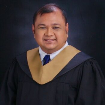 Meet the team: A man in a graduation gown and hood smiles against a dark background.
