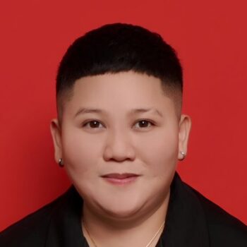 Meet the team: Person with short black hair and earrings, smiling in a black shirt on red background.