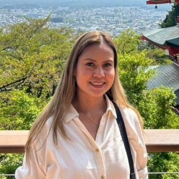 A woman smiles outdoors with greenery and city views—meet the team behind the scenes.