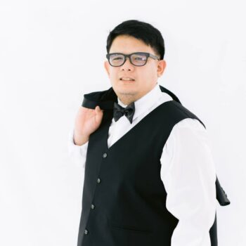 Meet the team: Man in a black vest and bow tie, holding a jacket over his shoulder.