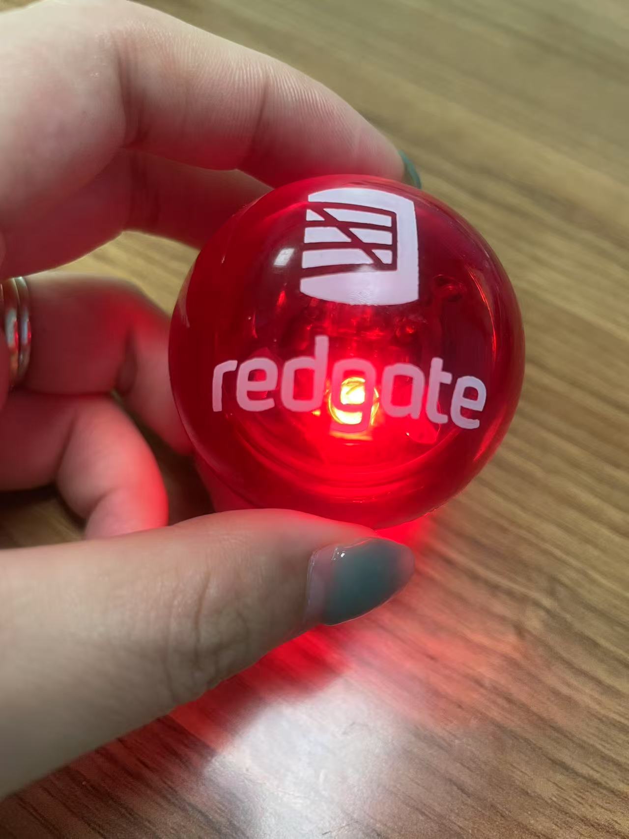 A hand holding a glowing red ball with the redgate logo on it.